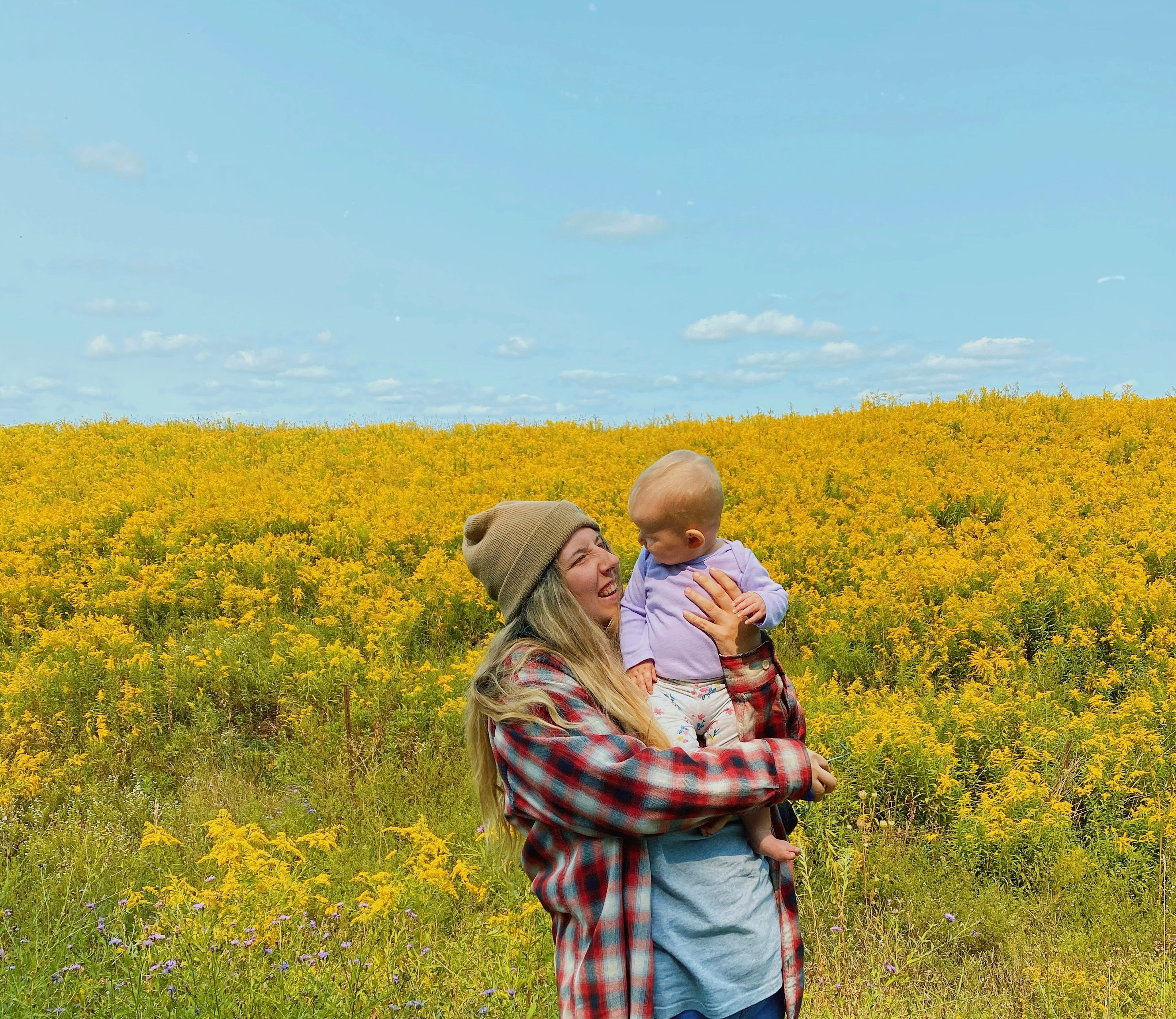 man in brown and white plaid shirt standing on yellow flower field during daytime